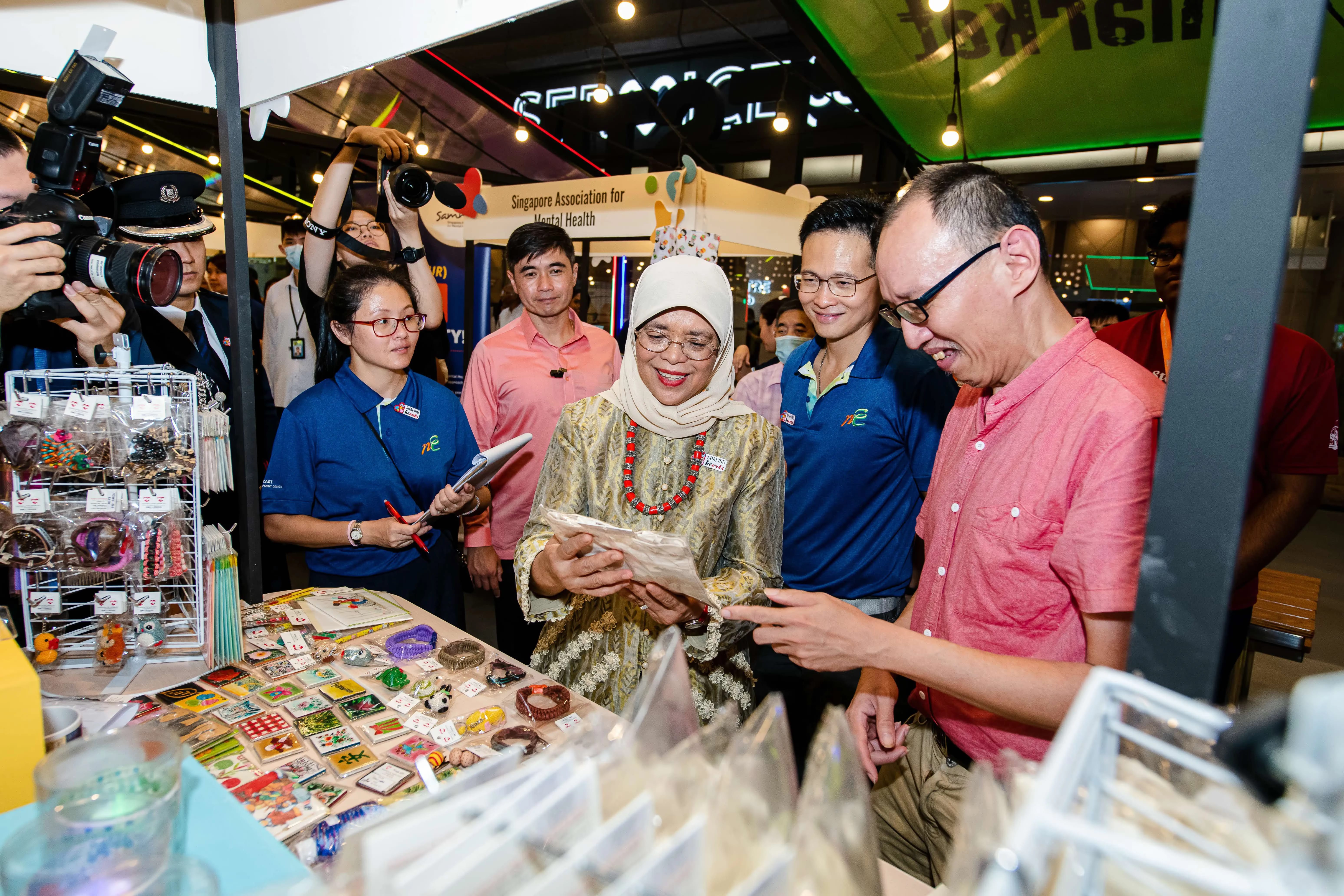  A group of people gather around a table displaying various colourful items at Shaping Hearts event booth.